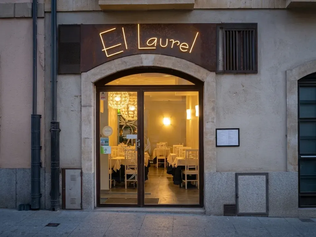Fachada de El Laurel al anochecer, con el letrero iluminado